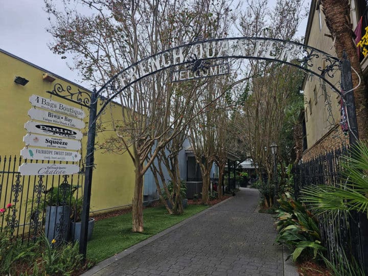 brick walkway under a curved sign with French Quarter welcome, small signs for Panini Pete's, Fairhope Sweet Shop, and other shops