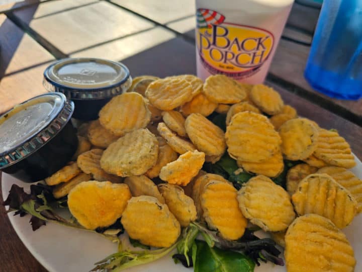 Fried pickles on a white plate next to a The Back Door cup