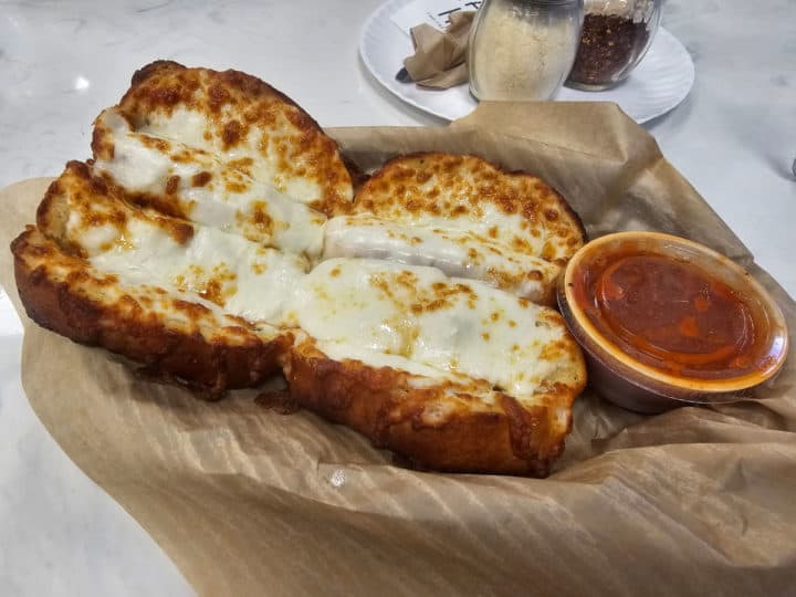 Garlic cheese bread next to a jar of marinara sauce on parchment paper