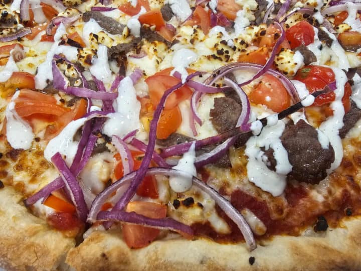 gyro meat, tomatoes, red onion, cheese, and sauce on a pizza