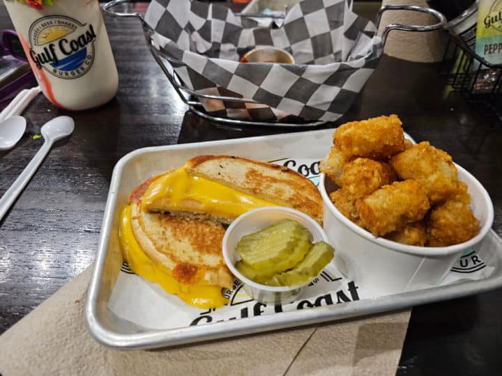 grilled cheese sandwich next to a cup of tater tots and a container of pickles