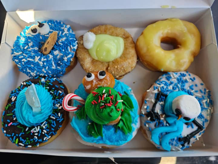 6 doughnuts in a white bakery box with a cookie monster donut, turtle, melted snowman, and shark doughnut