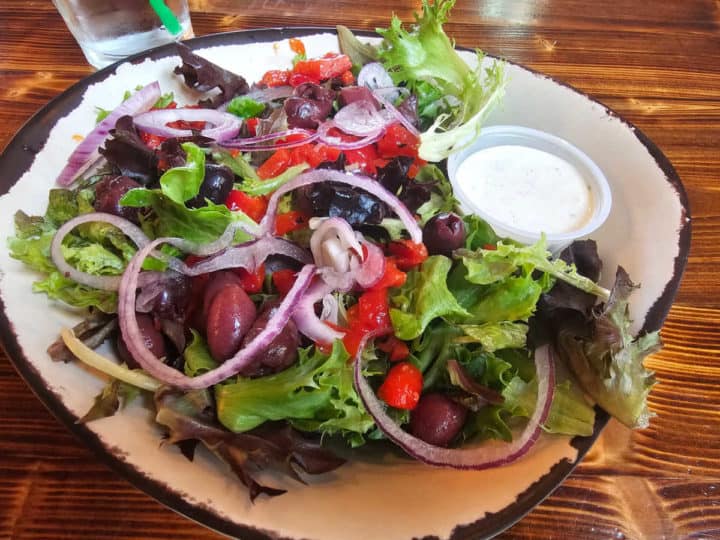 Salad with red onion, kalamata olives, tomatoes, and sauce on a white bowl plate