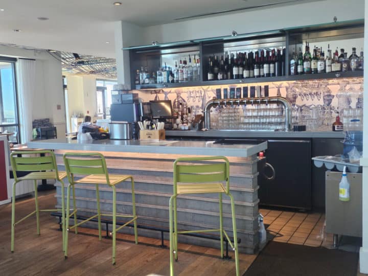 green bar stools at a small indoor bar with bottles and glassware