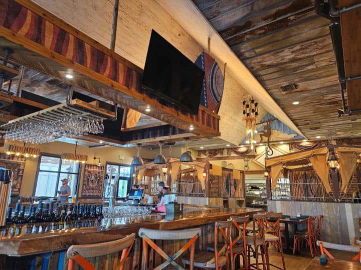 tall bar chairs next to a wooden bar with a tv overhead and African decorations