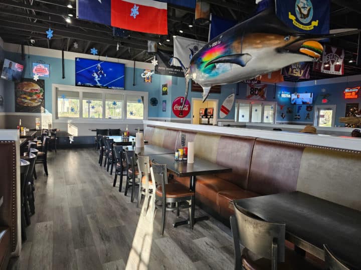 inside the restaurant with tables with chairs and bench seating, a large fish with a burger in its mouth, and flags hanging from the ceiling. 