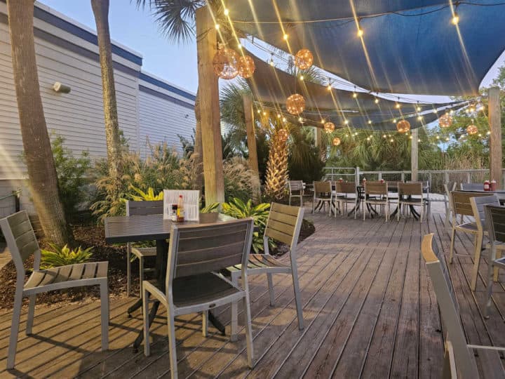 Outdoor tables and chairs under lights on a deck with blue awning