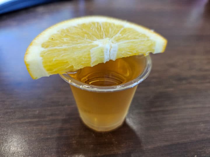 Plastic shot glass filled with a cocktail, lemon slice on top of glass
