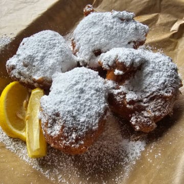 Beignets covered in powdered sugar with lemon slices on a parchment paper