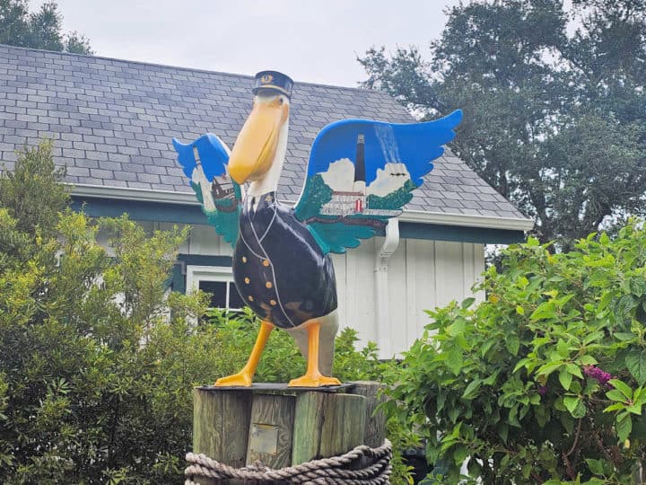 pelican statue with a lighthouse, blue angels and more painted on its wings sitting on wood posts