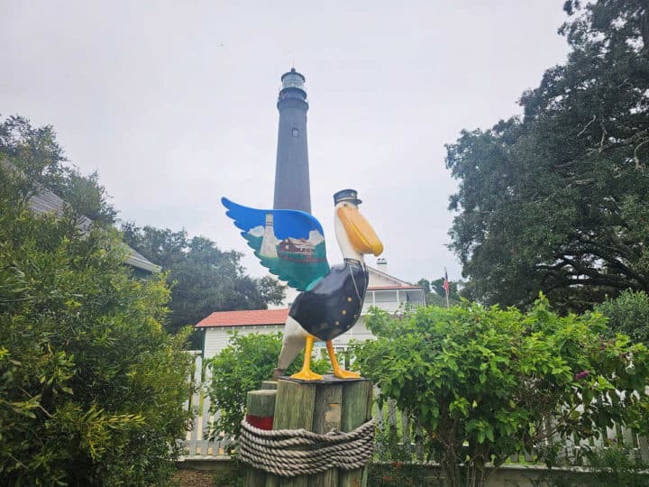 pelican statue below a lighthouse surrounded by greenery