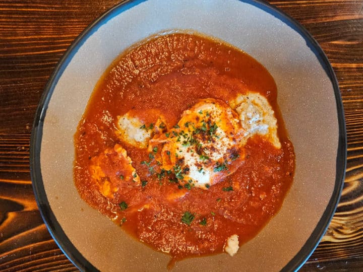 Shakshuka over grits with a poached egg in a bowl 