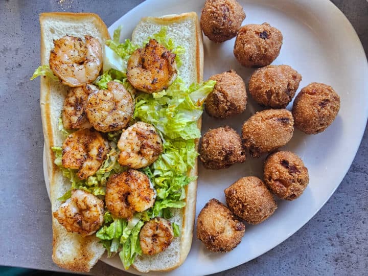 Shrimp po'boy with lettuce next to hushpuppies