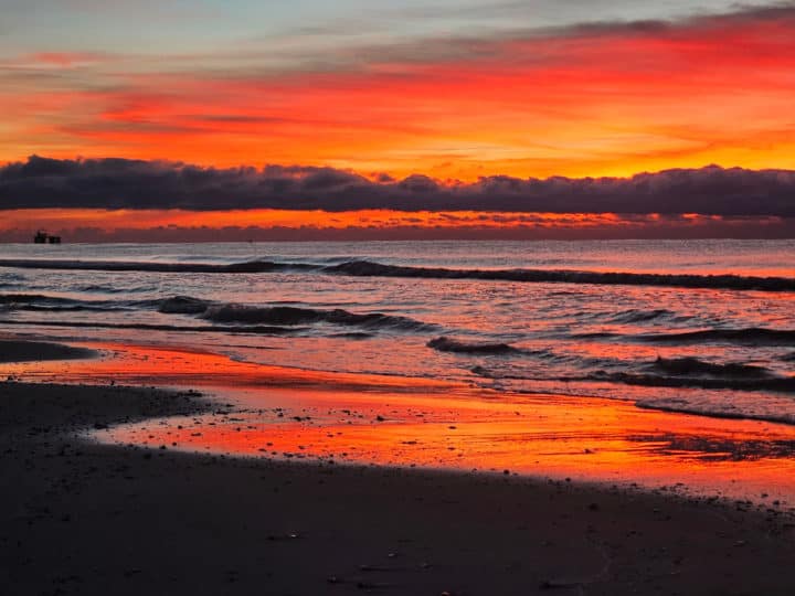 red and orange sunrise over clouds and waves breaking on the beach