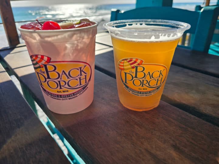 The Back Porch glasses with a cocktail and beer on a table with the ocean in the background