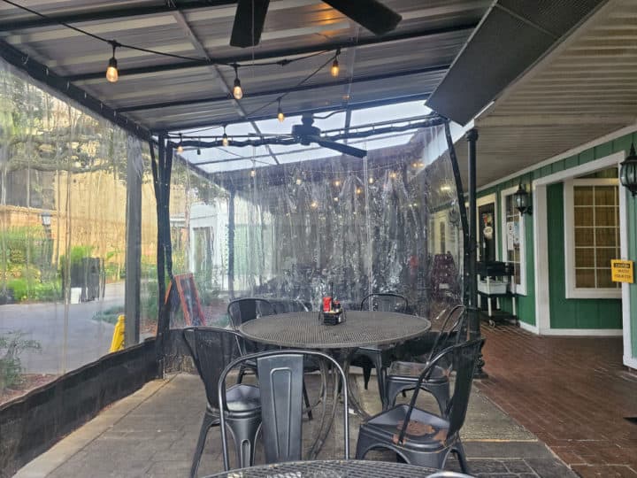 outdoor seating with tables and chairs behind a plastic rain cover