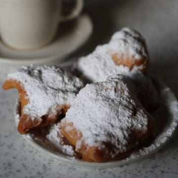 Three beignets on a white plate with a cup of coffee in the background