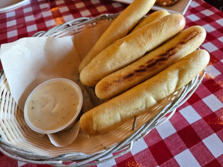 breadsticks and sauce in a basket on a red checkered tablecloth