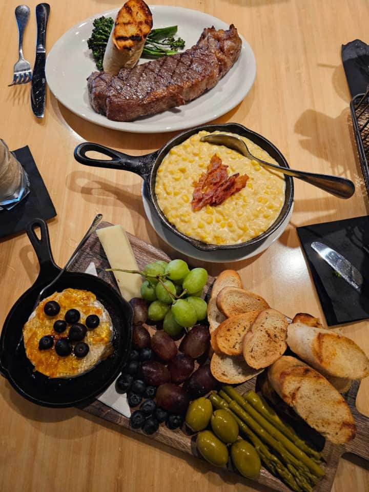 table with steak, corn, and baked brie dishes