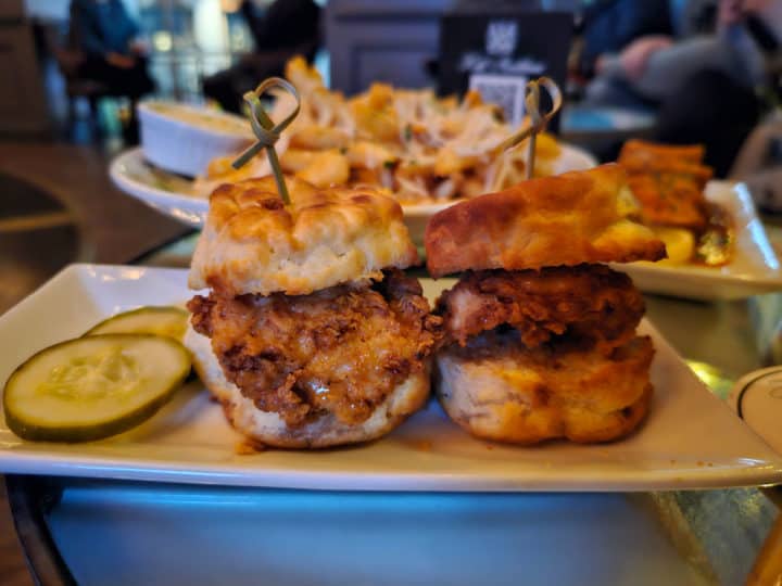 Two fried chicken sliders on biscuits with pickles on the side