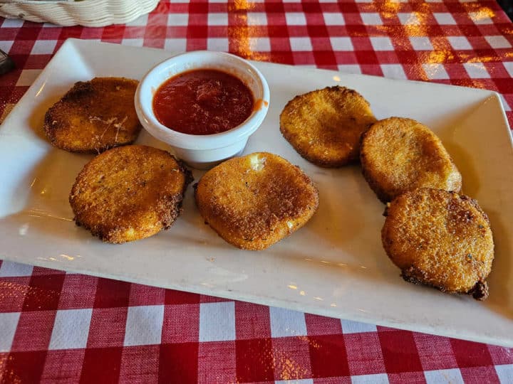 Fried mozzarella on a white plate with a container of marinara sauce
