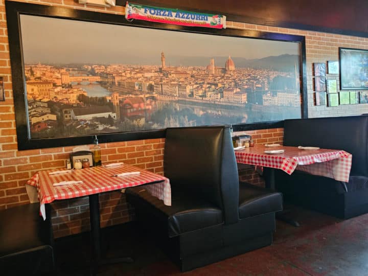 indoor booths with red checkered tablecloths under a large photo of Venice
