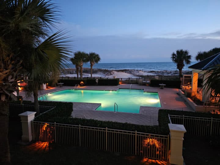 outdoor pool glowing with lights, palm trees, and the Gulf of Mexico and sand dunes