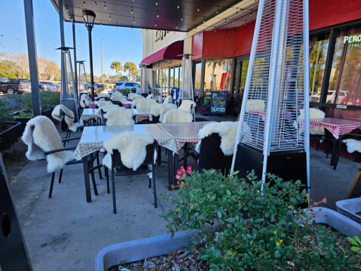 outdoor chairs covered in fake fur rugs next to tables and heat lamps