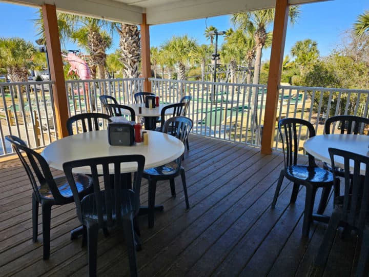 outdoor tables and chairs on a deck overlooking a mini golf course