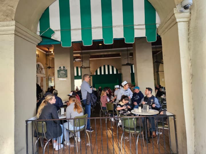 green and white awning over tables and people sitting enjoying beignets