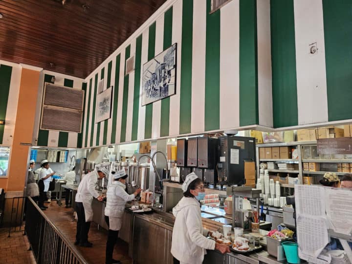 servers preparing trays with coffee and beignets below a green and white wall