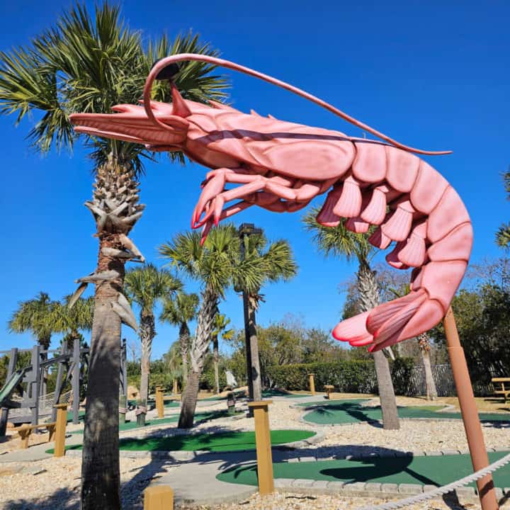 large pink shrimp sculpture next to a putt putt golf course