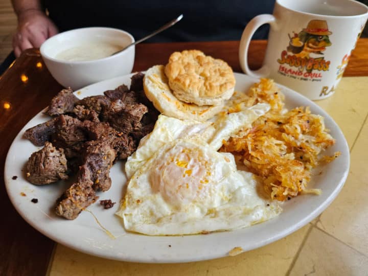 steak tips next to two eggs, a biscuit, and hashbrowns on a white plate. Sassy Bass Island Grill coffee mug