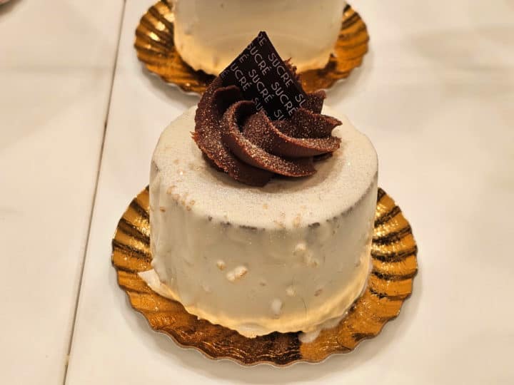 white chocolate patisserie with dark chocolate swirl on top and sucre chocolate square sitting on a gold foil circle