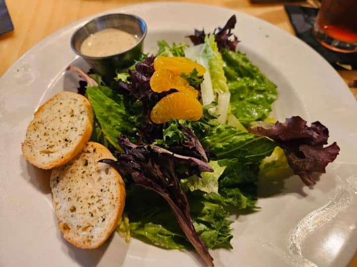 salad with mandarin orange segments, dressing in a container, and two slices of bread