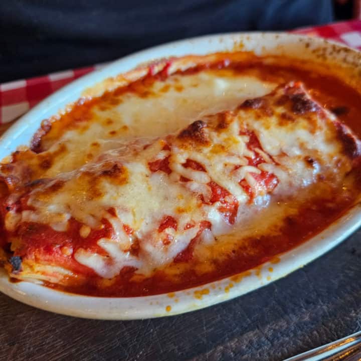 baked lasagna in a white platter on a checkered tablecloth