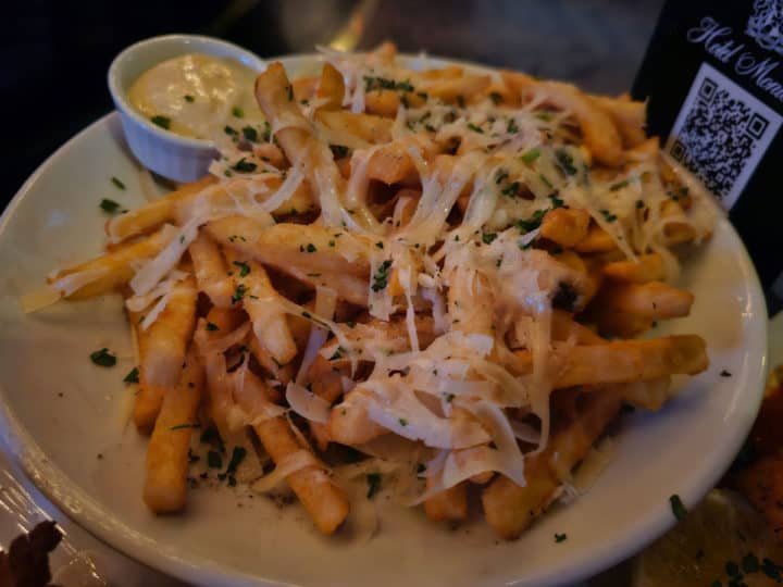 cheese covered truffle fries on a white plate with a small container of aioli 