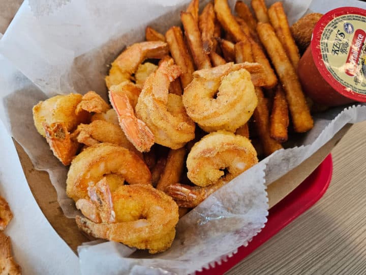 fried shrimp, french fries, and hushpuppies in a paper lined basket next to cocktail sauce