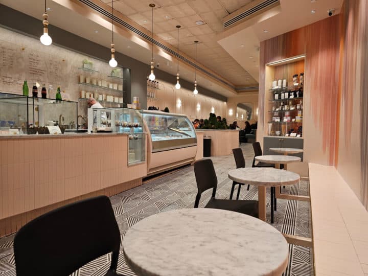 indoor seating along a bench with small circular tables, a bakery case, and pink wall