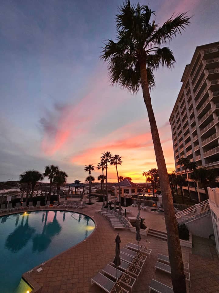 sunset sky over a pool next to a condo building with palm trees
