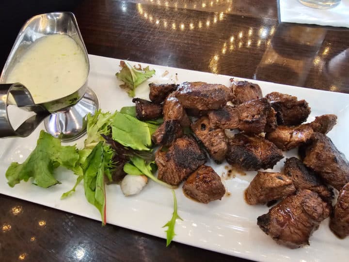 Beef tenderloin bites on a white platter next to a cream dipping sauce in a silver serving dish
