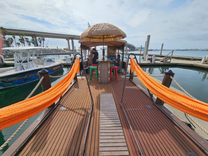 Orange hammocks hanging on a boat looking back to a tiki thatched roof, tiki bar and stools, and seating area