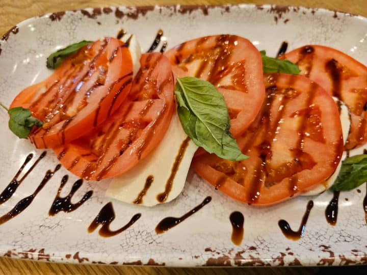 Caprese salad on a white plate with basil leaves on top