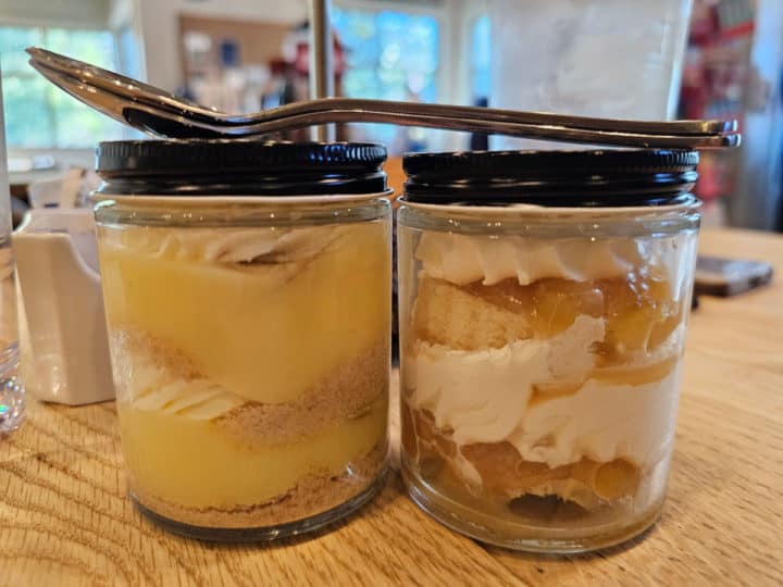 two jars with desserts in them and spoons on top of the jars