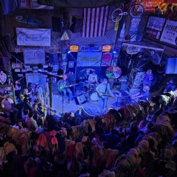 Looking down at a band with Flora Bama sign, American flag, and bras hanging from the ceiling