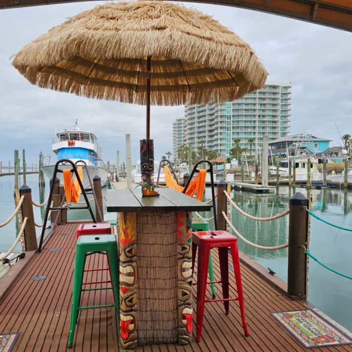 Pontoon boat with tiki bar and stools, hammocks, and tiki decorations on the water. 