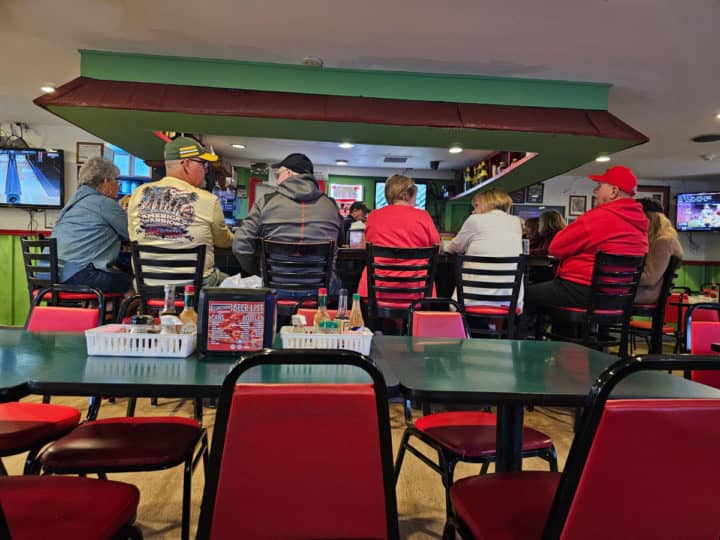 people sitting on bar stools around a bar with tv's in the background