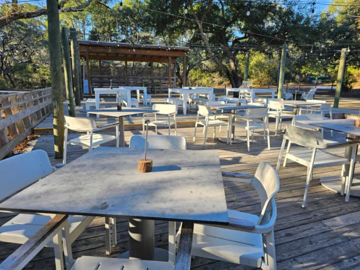 outdoor seating area with tables and white chairs, music stage in the background