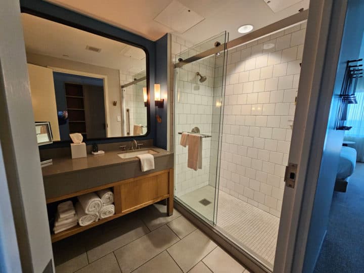bathroom with large mirror, sink and tables, walk in shower with glass doors