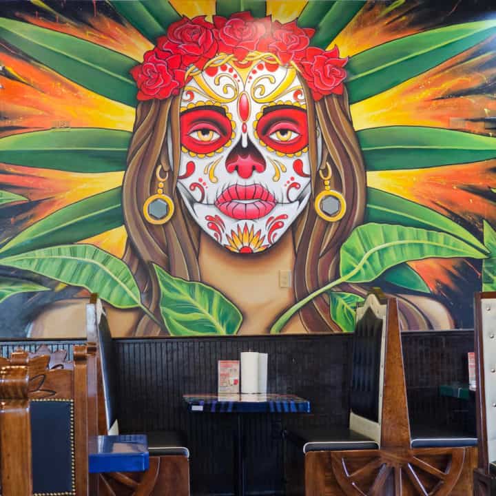 Mural above a table with a women painted for the day of the dead. 